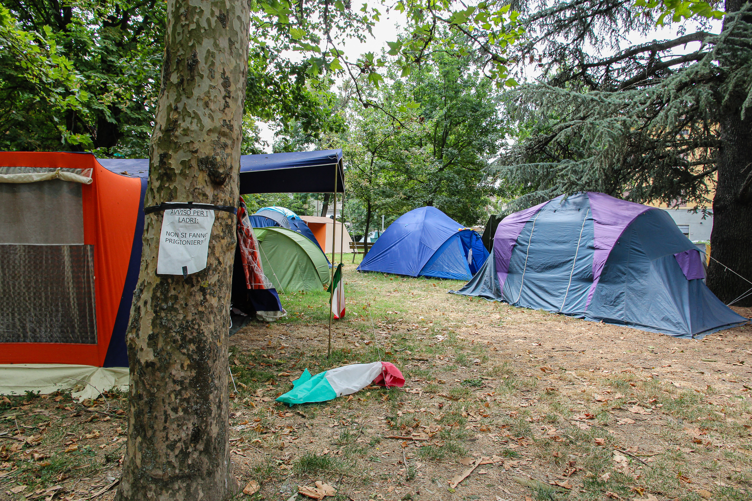 Im Park stehen Campingzelte, davor liegt eine italienische Fahne im Gras